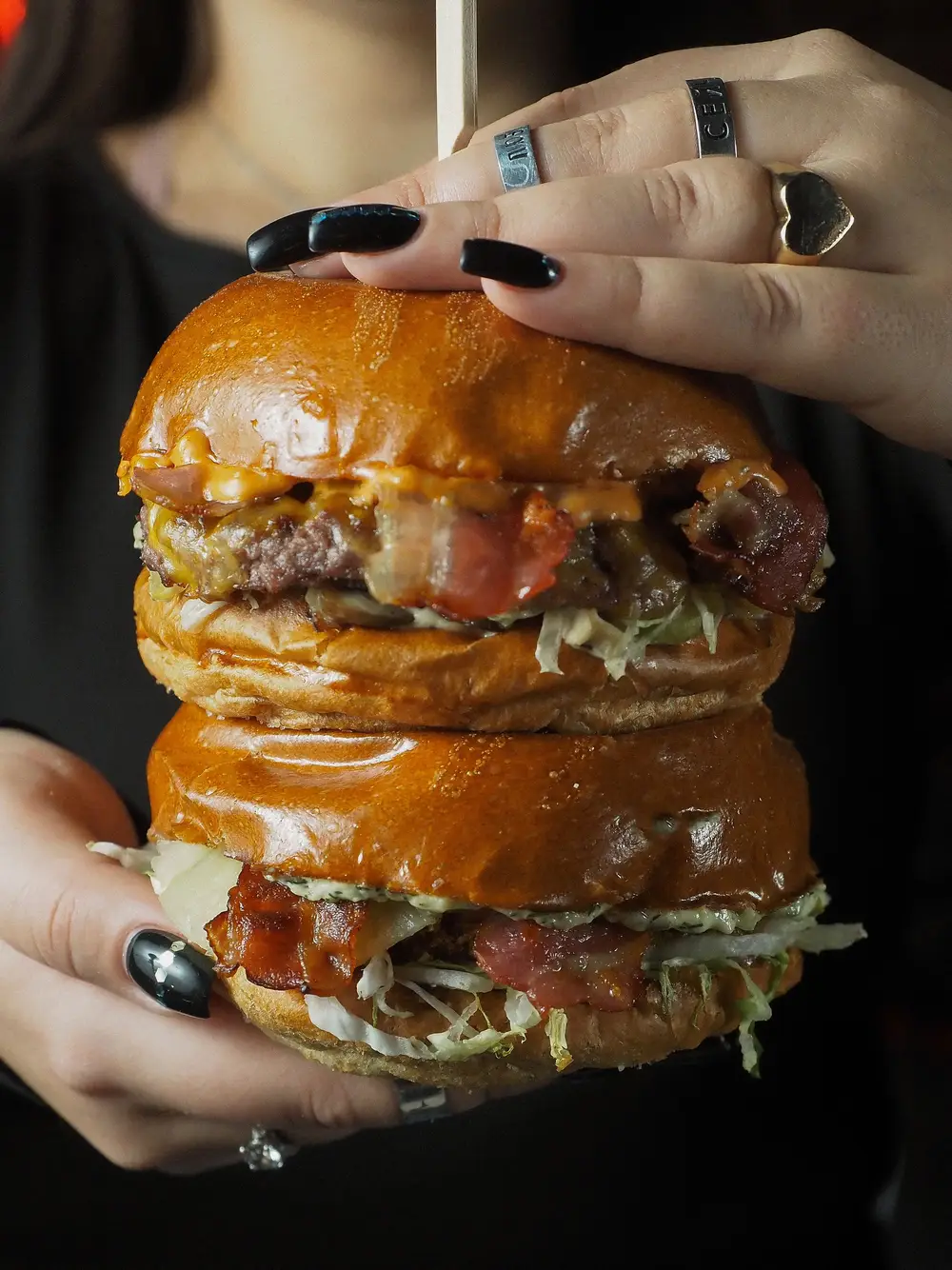 Mãos a segurar um smash burger duplo com bacon