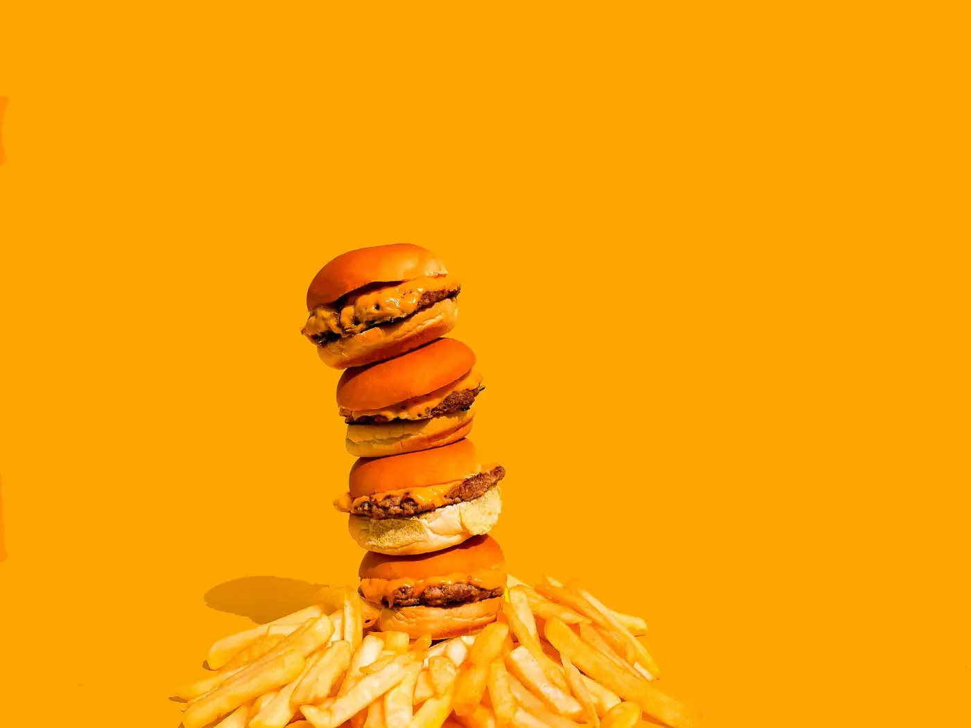 Torre de mini burgers sobre batatas, em fundo laranja