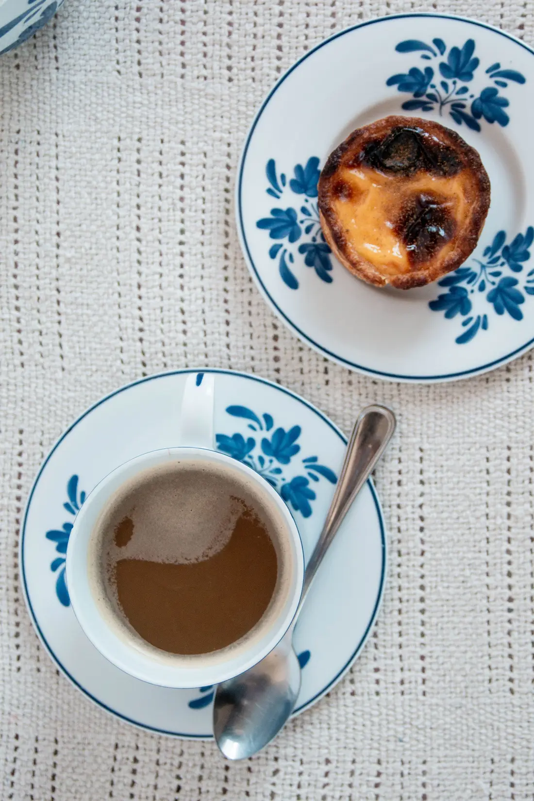 Café em chávenas de porcelana azul e branca, com um pastel de nata