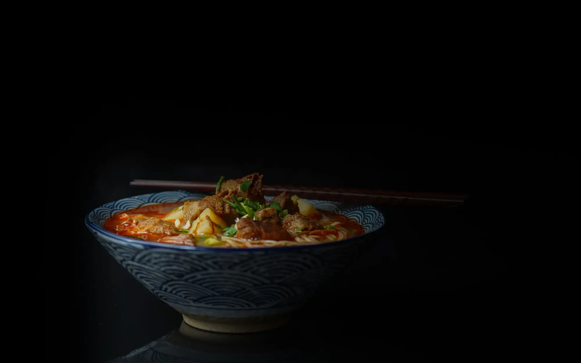 Taça de ramen picante sobre fundo escuro, com pauzinhos