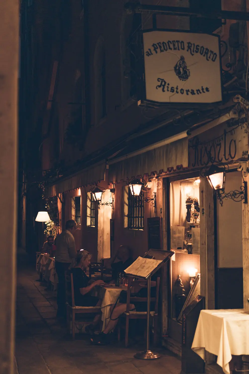 Rua estreita à noite, com a porta iluminada da trattoria