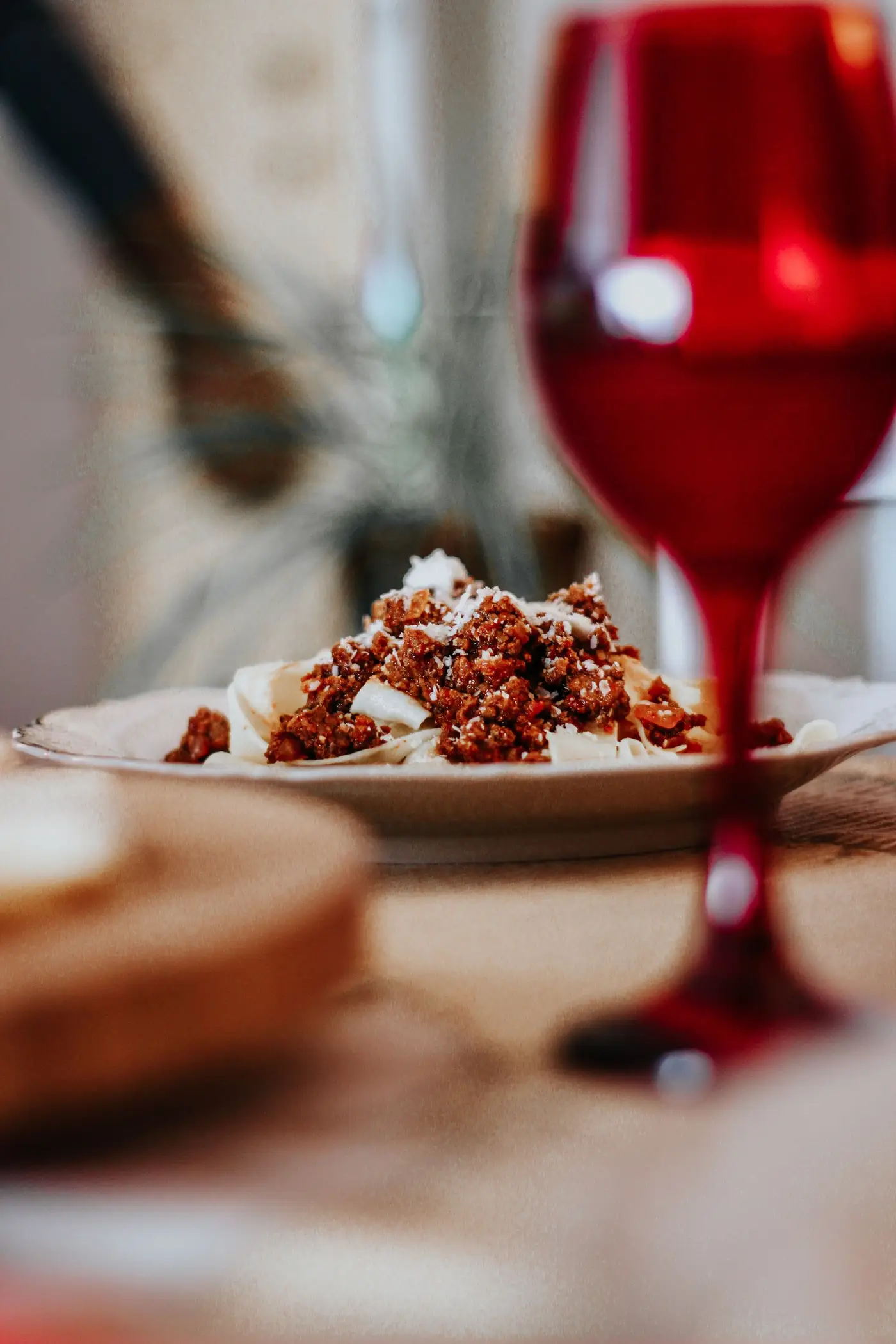 Copo de vinho tinto diante de um prato de massa com ragù