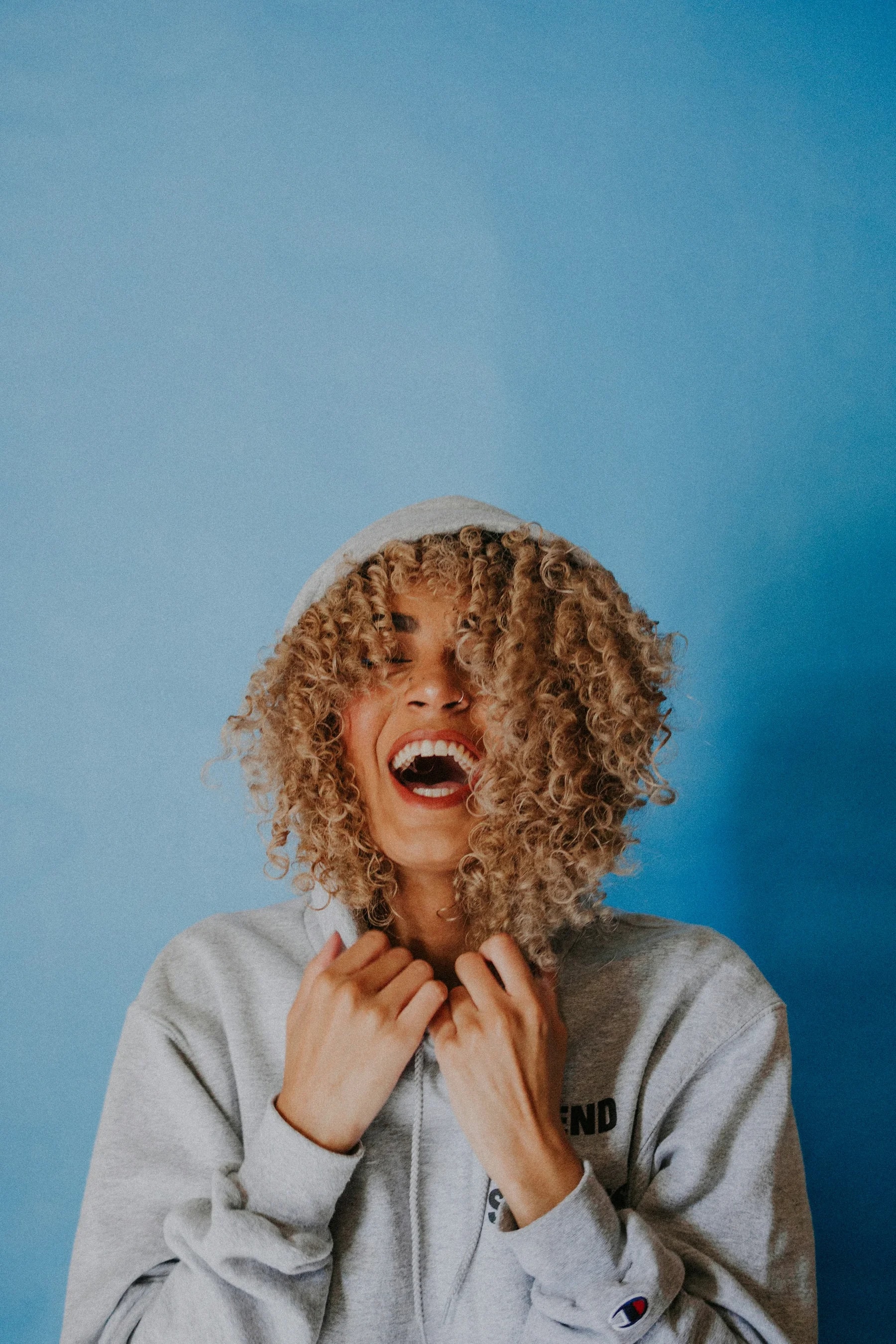 Jovem de cabelo encaracolado a rir contra uma parede azul