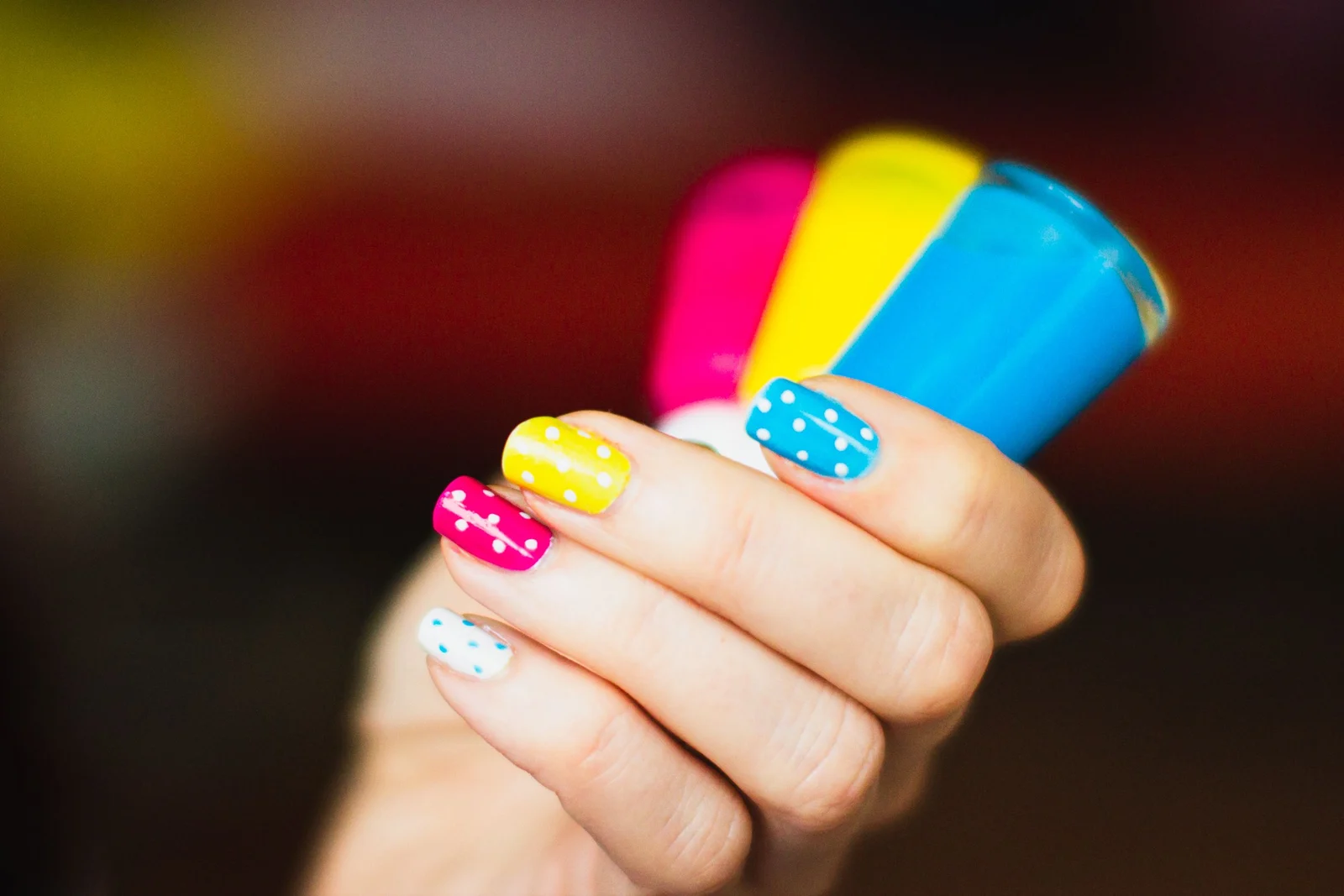 Unhas coloridas em amarelo, rosa e azul